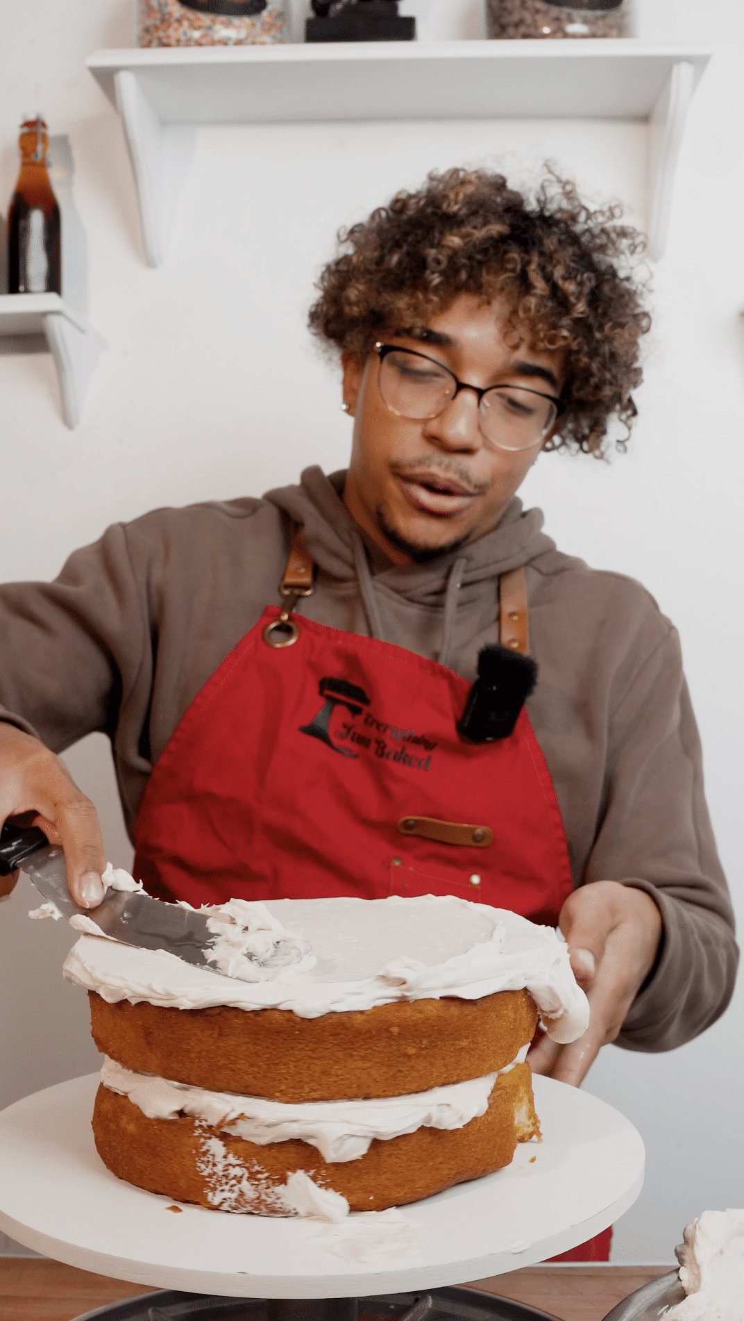 Baker adding buttercream frosting between two round cake layers.